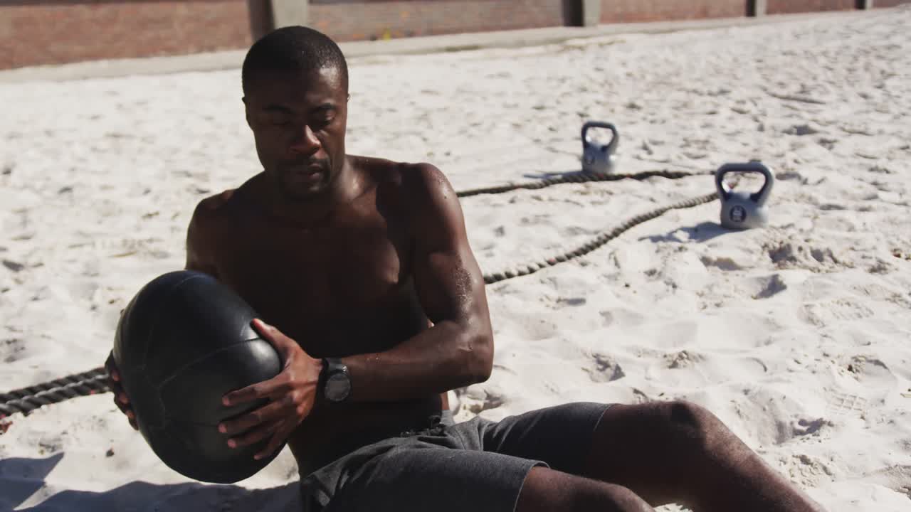 Focused african american man doing twists with ball, exercising outdoors on beach
