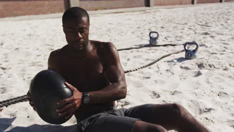 Focused-african-american-man-doing-twists-with-ball,-exercising-outdoors-on-beach