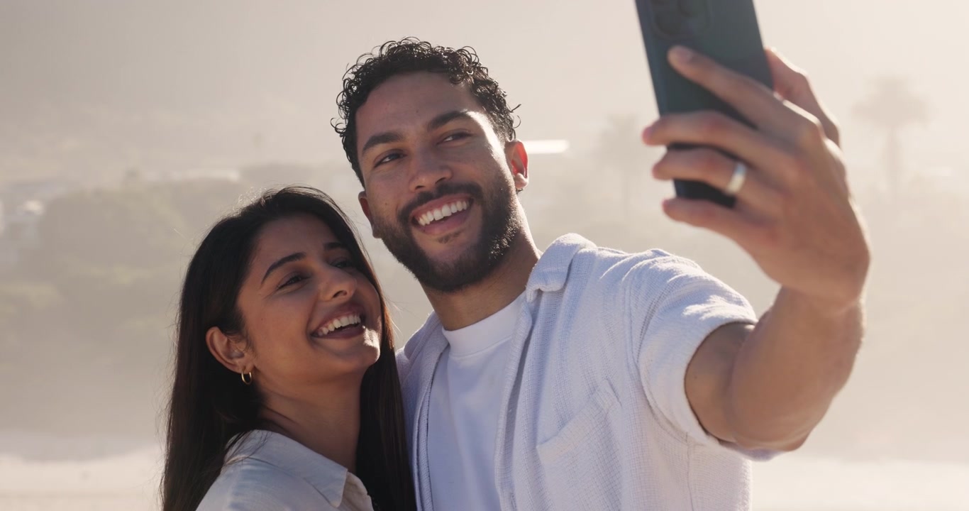 Giovane coppia che si scatta un selfie in spiaggia al tramonto