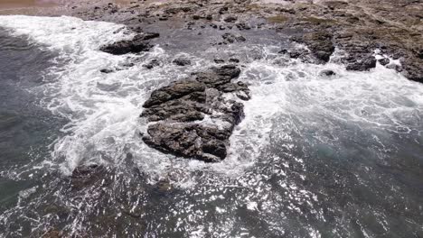 Static-Aerial-Close-up-Shot-Of-The-Sea-Washing-Up-Against-The-Rocks-And-Beach