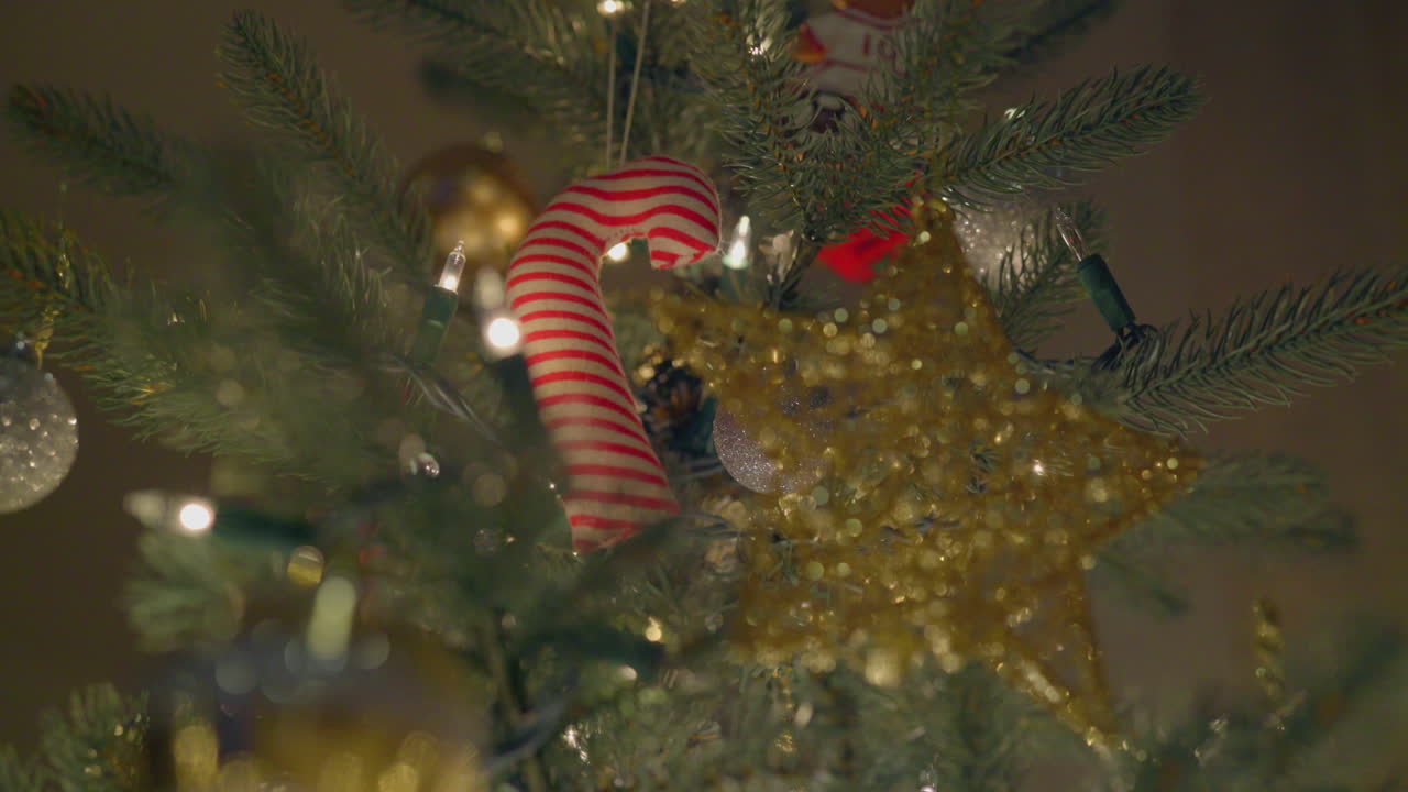 un adorno de bastón de caramelo cuelga de un árbol de navidad junto con otros adornos y luces navideñas intermitentes