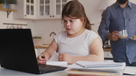 girl doing online homework with dad in kitchen