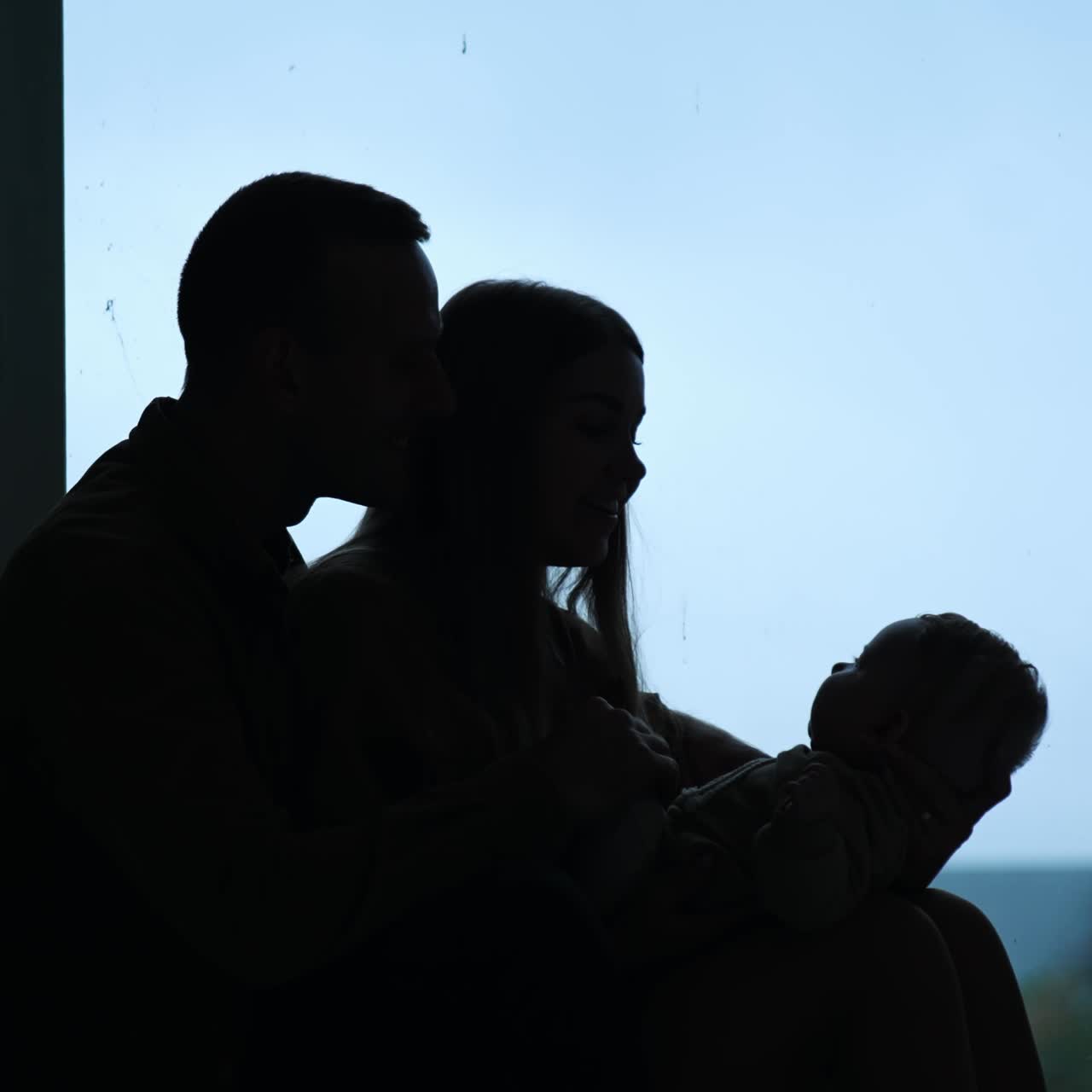 Genitori felici che tengono in braccio un bambino seduti vicino alla finestra. Silhouette di genitori affettuosi insieme al loro bambino