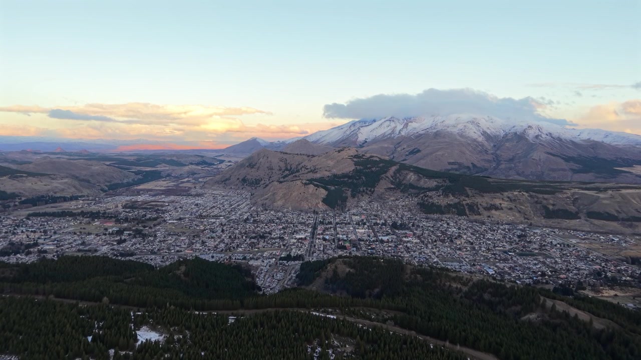 Drone sobe sobre a cidade de Esquel na hora dourada com picos andinos nevados ao fundo