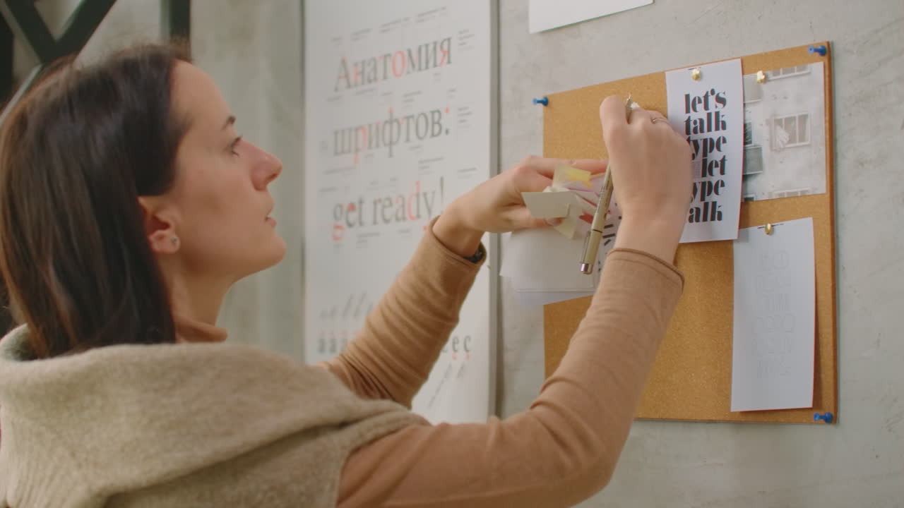una mujer diseñadora de pie en la pared adjunta sus ideas a la selección de colores de la pared y la colorística. eligiendo un color y preparándose para crear una solución de diseño y color.