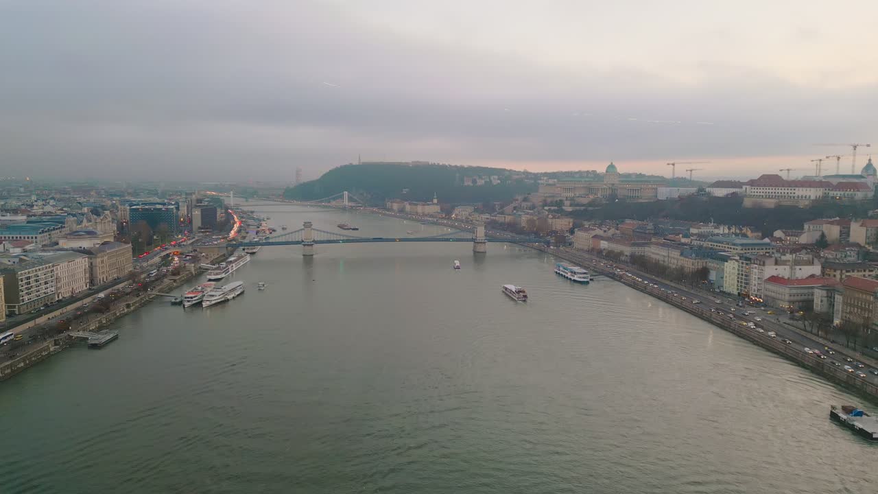 Filmato drone che mostra un avanzamento lungo il fiume Danubio verso il Ponte delle Catene Széchenyi, mentre navi da crociera solcano il fiume.