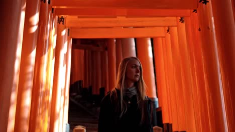 a woman stands in the serene beauty of fushimi inari shrine at sunrise, surrounded by the iconic vermilion torii gates.