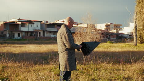 elderly man closes and reopens the umbrella on a sunny winter day