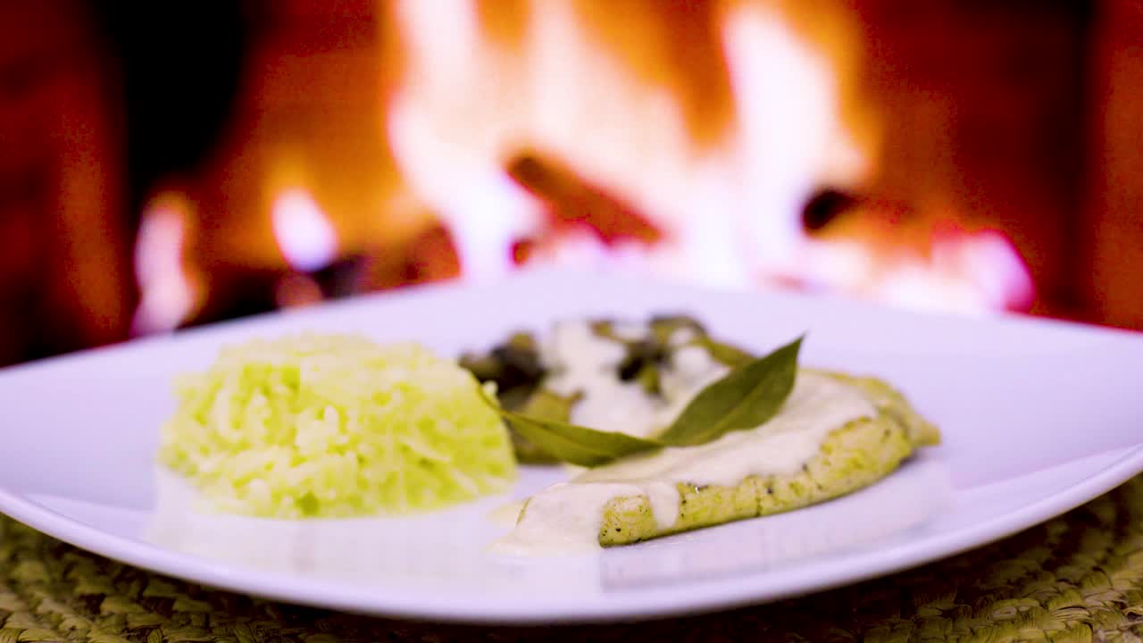 chuleta de pollo con crema y hongos, crema fresca, queso, arroz en un plato cuadrado con un fuego de leña en el fondo