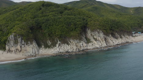 Bird-eye-view-of-a-steep-cliff-sea-coast-with-with-green-forest-hills-on-top