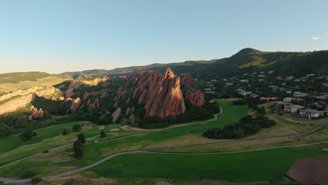 aerial flyover of green golf course bordered by natural red rock cliffs in colorado summer, ascend establishing
