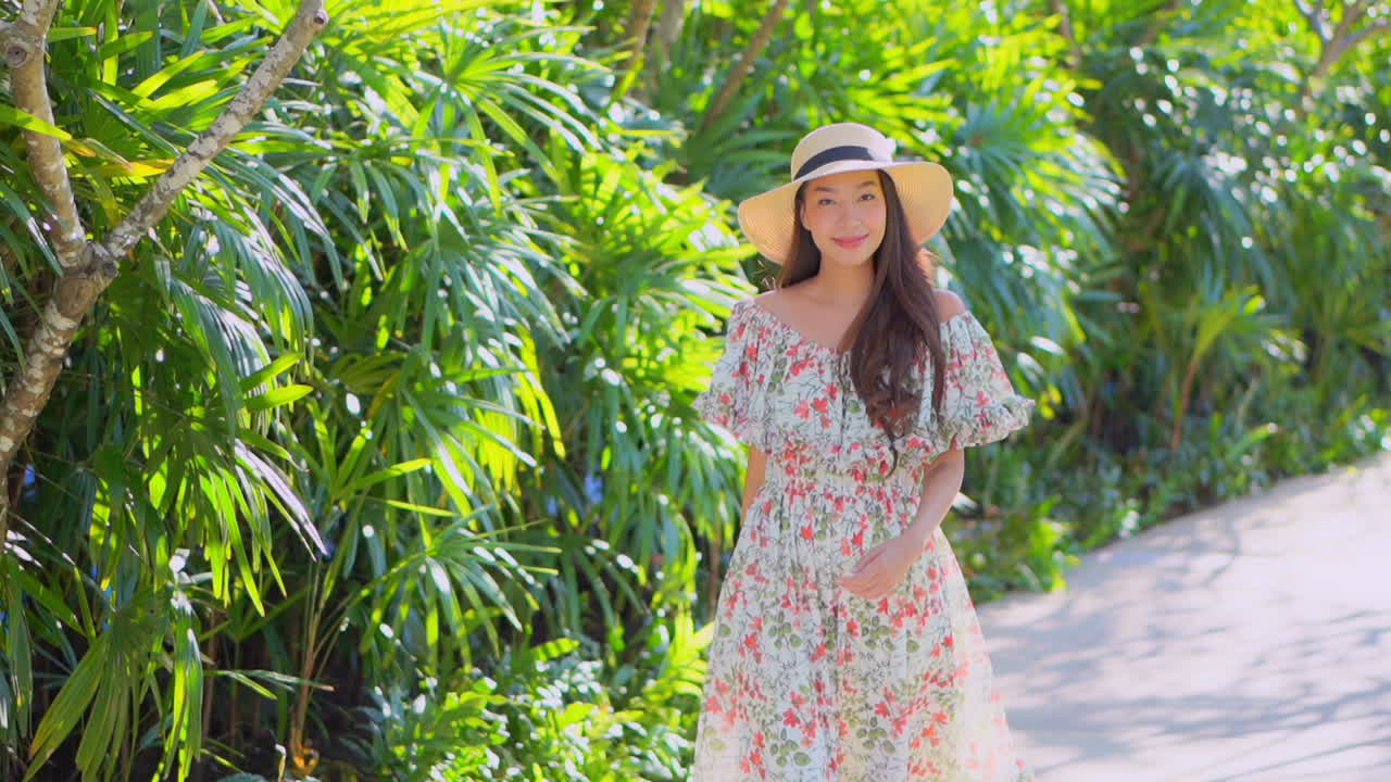 Girl walks beside palm bushes wearing flowery vacation dress and hat
