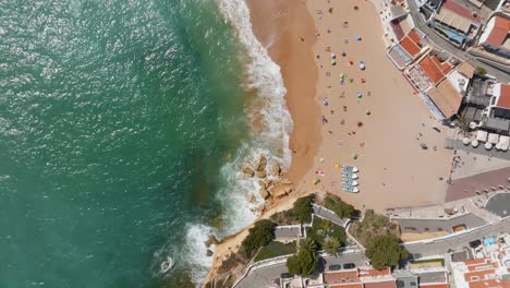 coastline waves crashing on tourists on beach, carvoeiro village, drone top down bird's eye view pan