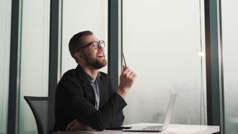 a cheerful man in a business suit is thinking while sitting at a laptop