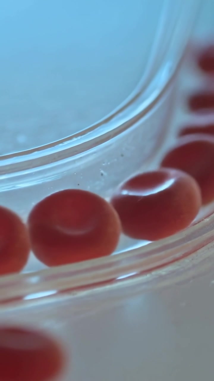 Vertical video: Shifting shot nudging red pellets rolling along clear ridge on flat surface, dust