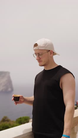 vertical shot of caucasian male drink black coffee on scenic balcony, mallorca