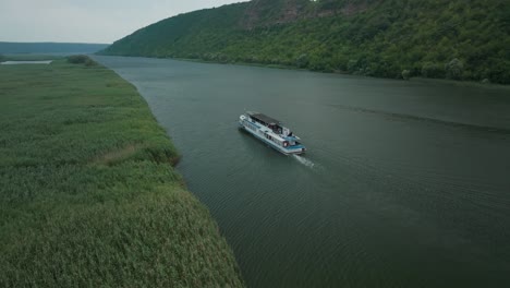 rlateral movement escort boat, behind a boat that moves on a river next to tall grass through high mountains to the side horizon