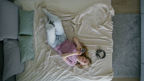 woman relaxing on bed with phone and headphones