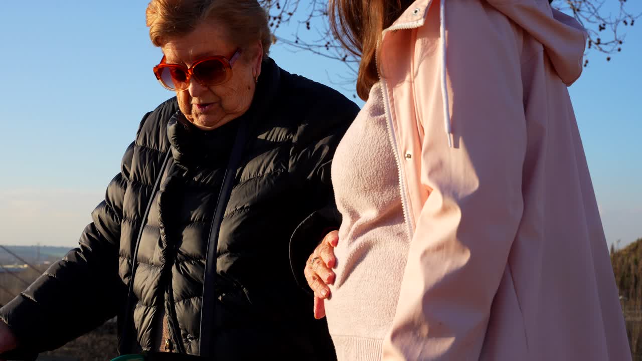 Happy grandma touching the belly of her pregnant daughter in the park