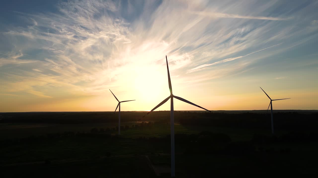 Large wind turbines with blades in field aerial view bright orange sunset blue sky wind park slow motion drone turn