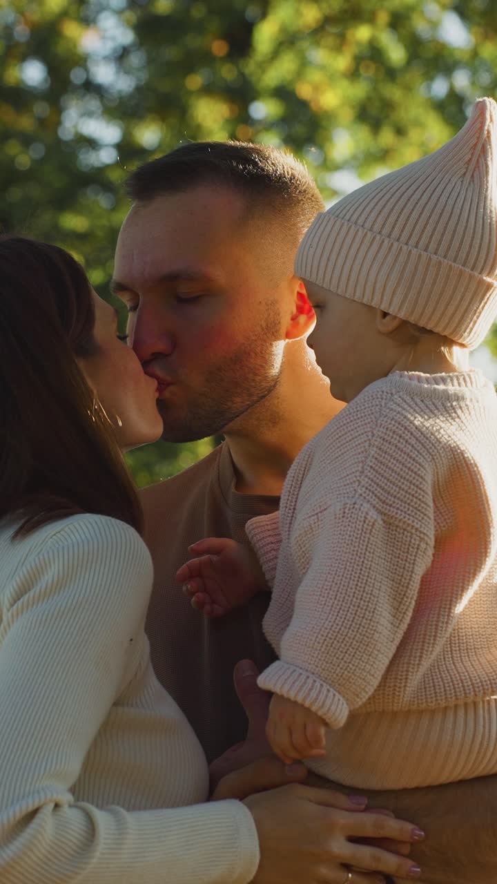 Genitori amorevoli che si baciano mentre tengono in braccio il loro bambino in un parco soleggiato