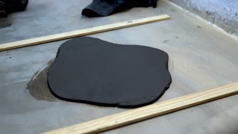 Flattening dark clay with wood roller on ceramic workshop table with height guides by hand, Handheld close up shot