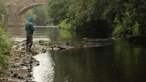 disparo de mano de un pescador de mosca pescando y caminando a lo largo de una orilla del río