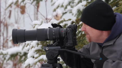 Male-photographer-dressed-for-winter-cold-looks-through-camera-lens