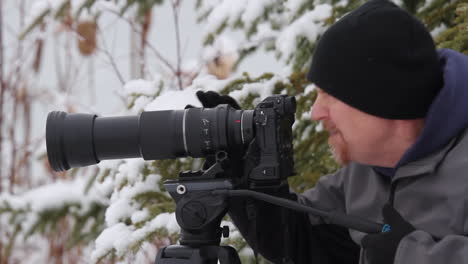 fotografo maschio vestito per il freddo invernale guarda attraverso l'obiettivo della telecamera