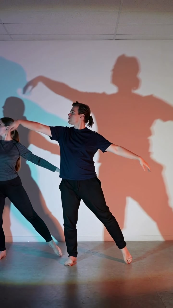 Vertical video: Starting rehearsal two barefoot dancers moving in studio with cyan-orange light