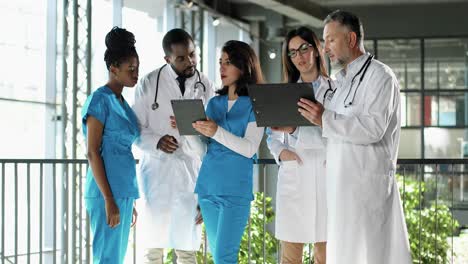 multi ethnic doctors, men and women, standing in hospital, talking and discussing diagnosis using folders and tablet device