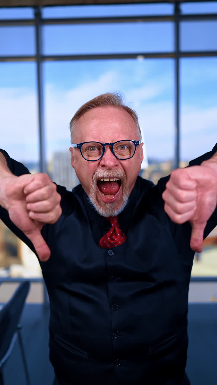 Angry senior male in black clothes with red tie showing thumbs down. Irritated dissatisfied boss in office. Vertical video.