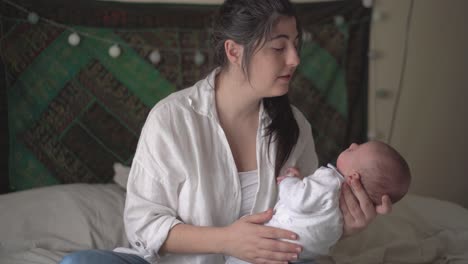 smiling mother talking to newborn baby at home