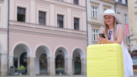 nice video of a cute tourist girl waiting leaning on a yellow suitcase. a tourist during a trip to a european city. the traveler is looking at the phone