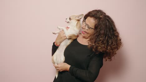 middle age woman smiling confident hugging chihuahua over pink background