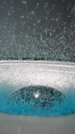 blue granules of food coloring bounce and stir lying on diaphragm of speaker. vibration and sound waves move fine crystalline substance on dark background macro