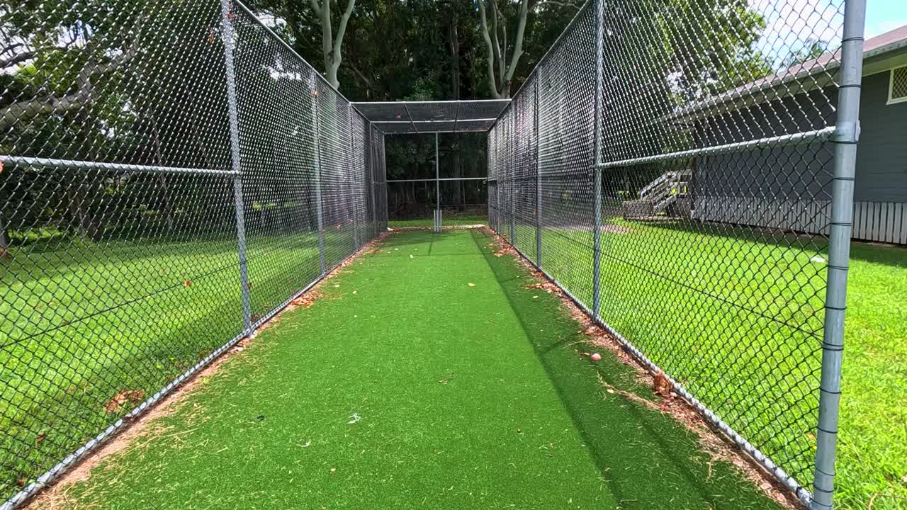 Aerial view of a cricket net in a sunny outdoor setting, showcasing the approach and environment in vibrant daylight