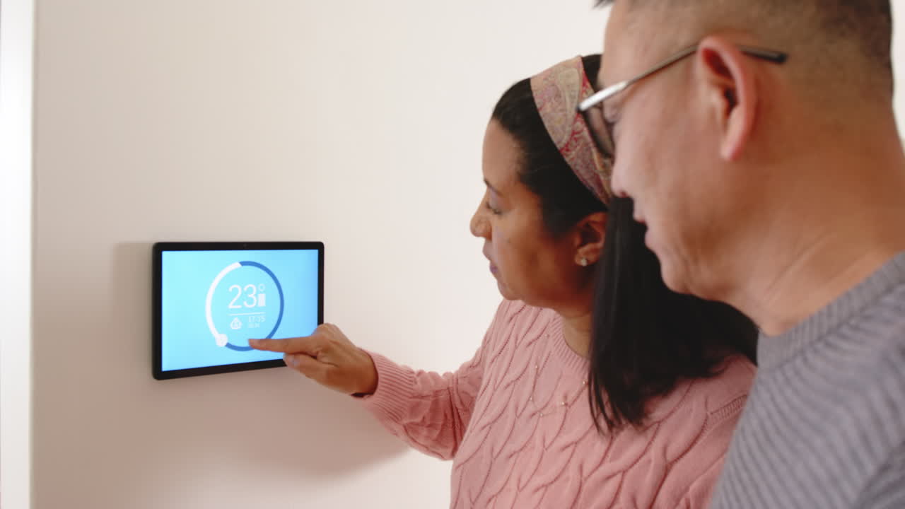 Senior asian couple adjusting smart thermostat at home, managing energy efficiently