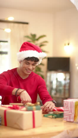 vertical video of biracial man wrapping christmas present in decorative paper at home, slow motion