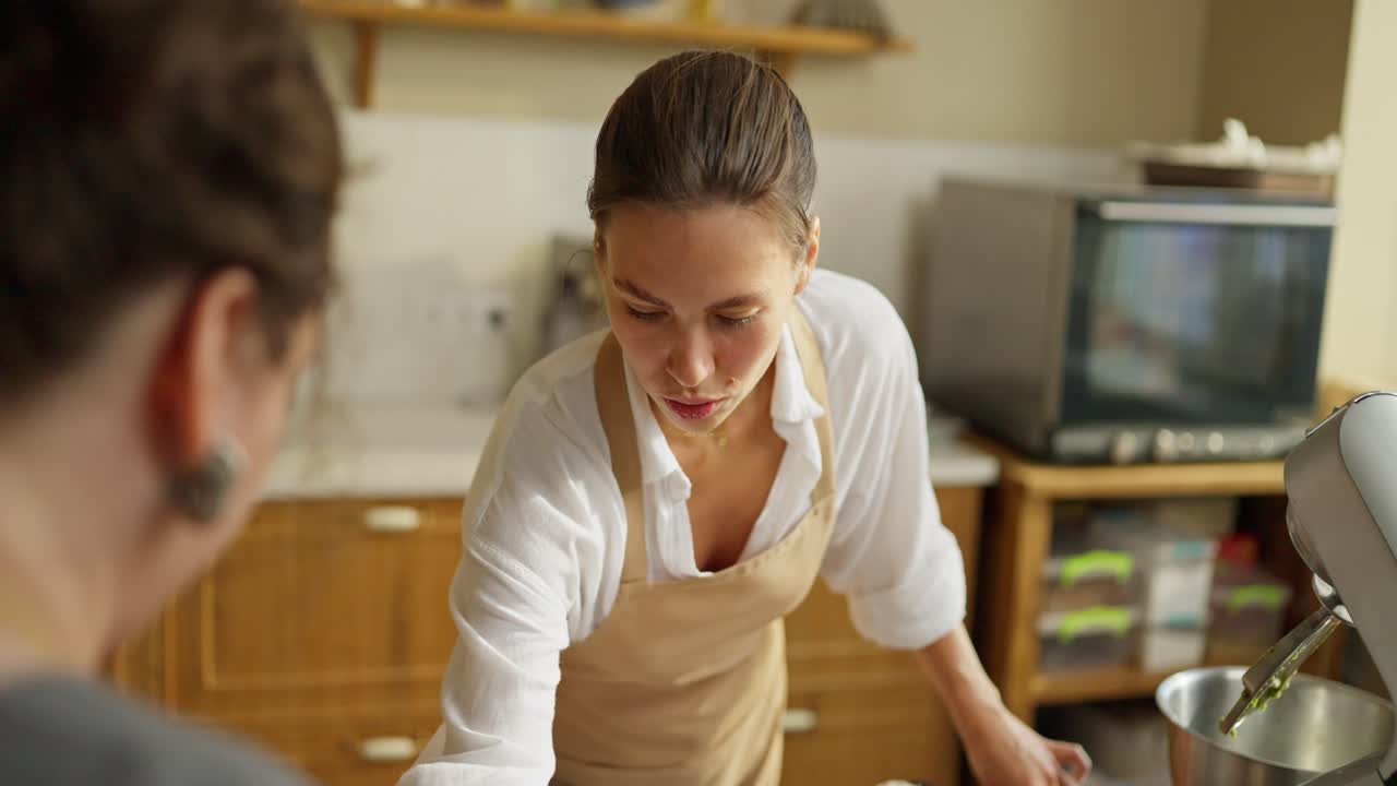 Una donna con una camicia bianca e un grembiule marrone prepara dolci in cucina