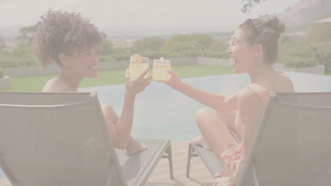 Two women lounging infinity pool left raising glass starting toast clinking sipping relaxing travel
