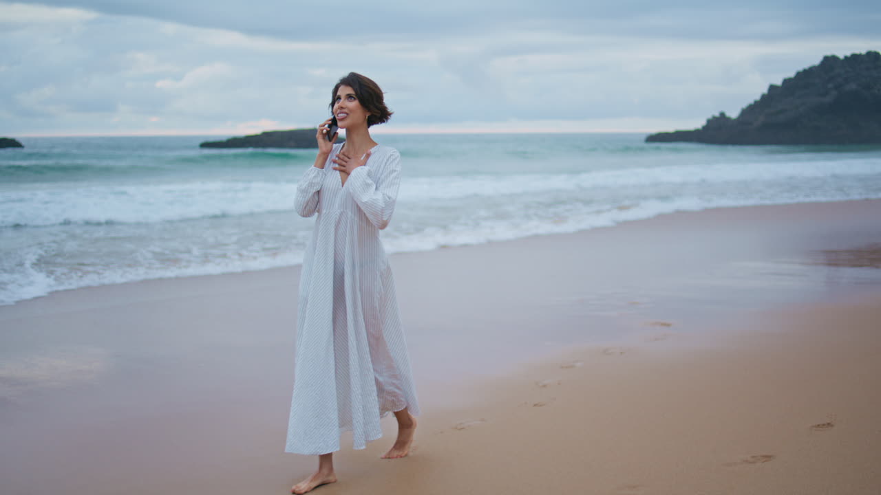 una chica despreocupada hablando con su teléfono inteligente en una hermosa playa del océano.