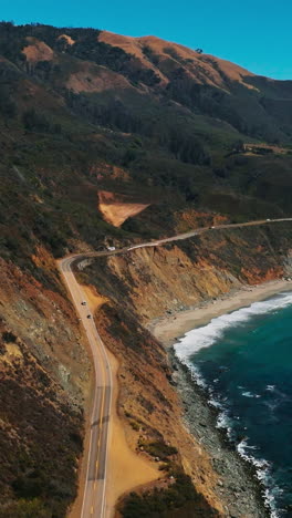 road along the sloping mountainous coast of pacific in california. amazing scenery of the shoreline on sunny hot day. top view. vertical video