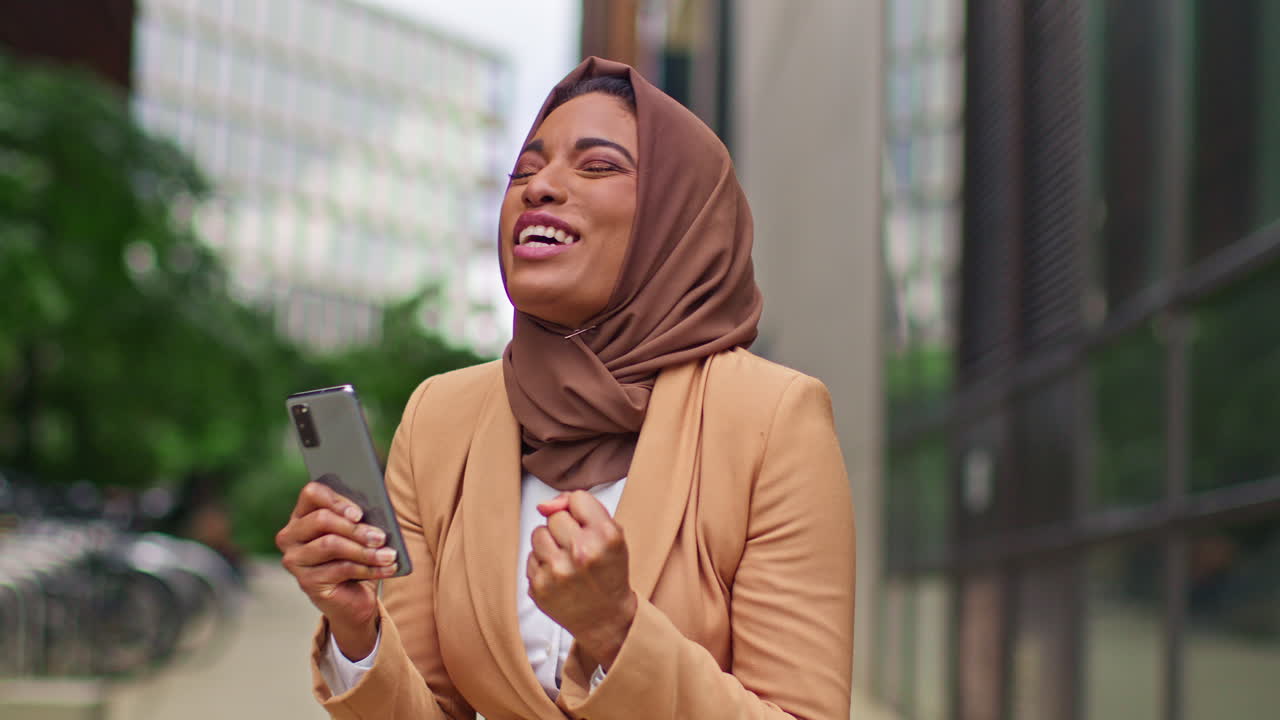 Muslim Businesswoman Wearing Hijab Standing Outside Modern Office Getting Good News About Job Offer Or Promotion On Mobile Phone 5