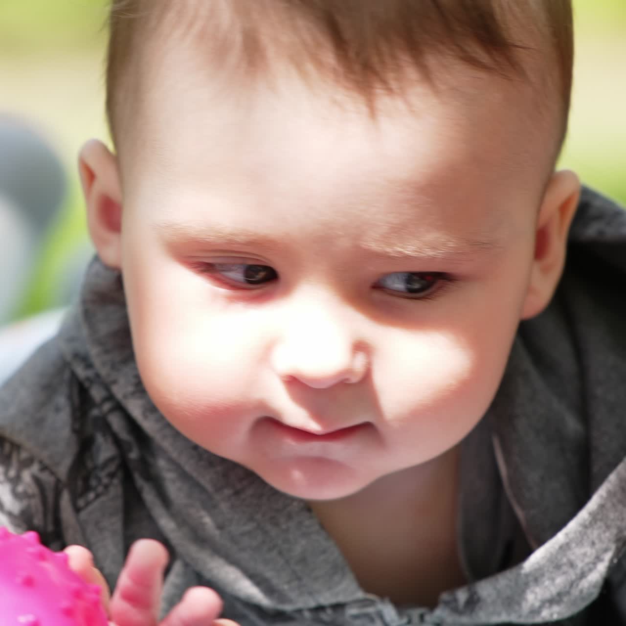 Adorable active baby boy wearing grey shirt lies in nature. Funny boy waving hands and feet. Close up. Blurred backdrop