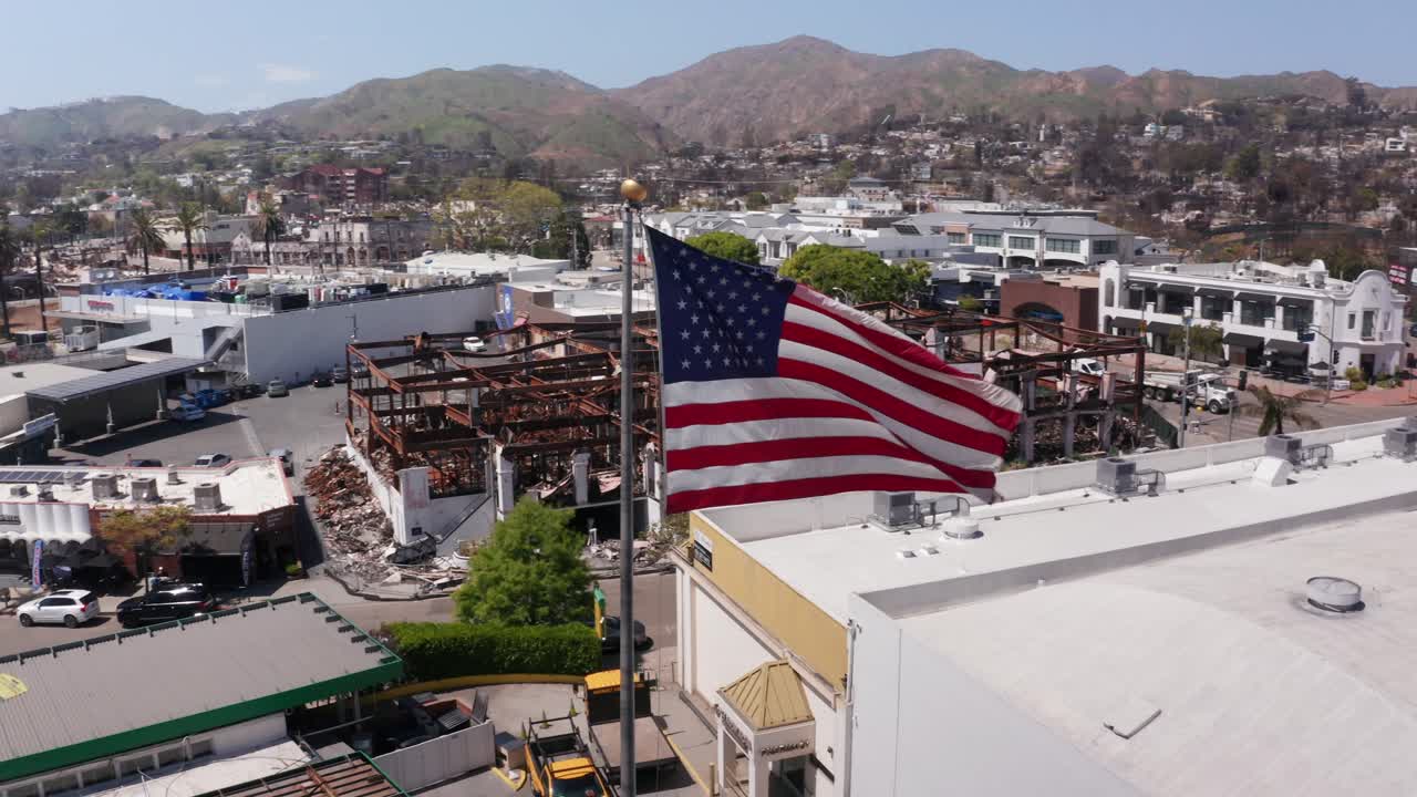 Aerial close-up panning shot of an American flag on Sunset Blvd. surrounded by the damage of the Palisades Fire in Los Angeles, California. 4K