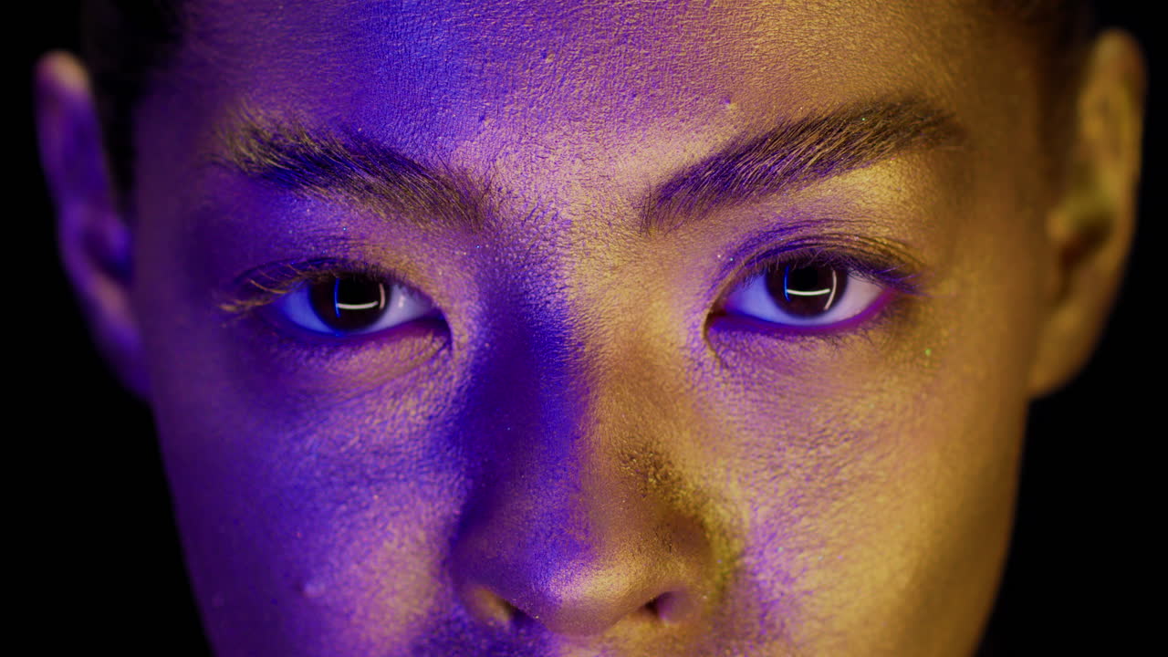 Close-up portrait of a woman with gold and purple makeup