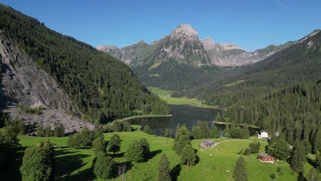 scenic nature landscape of swiss wooden cabin chalet farm on green alpine meadow surrounded by alp background mountains pine trees overlook turquoise glacier lake in a sunny day in europe switzerland