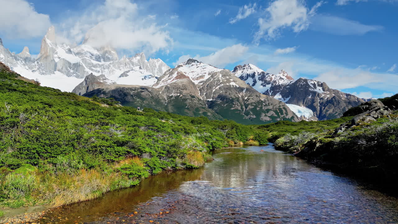 Ripresa aerea con drone di un fiume calmo che riflette le cime innevate del Fitz Roy sotto un cielo azzurro in slow motion