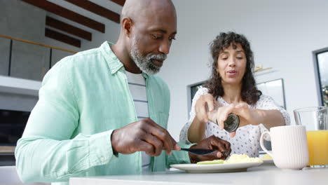 Happy-biracial-couple-having-breakfast-and-seasoning-scrambled-eggs-in-kitchen,-slow-motion